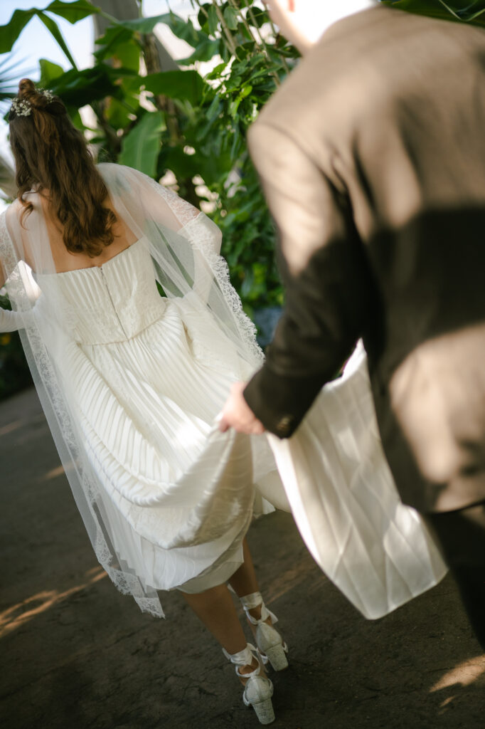 Groom holding brides dress as they walk from first look