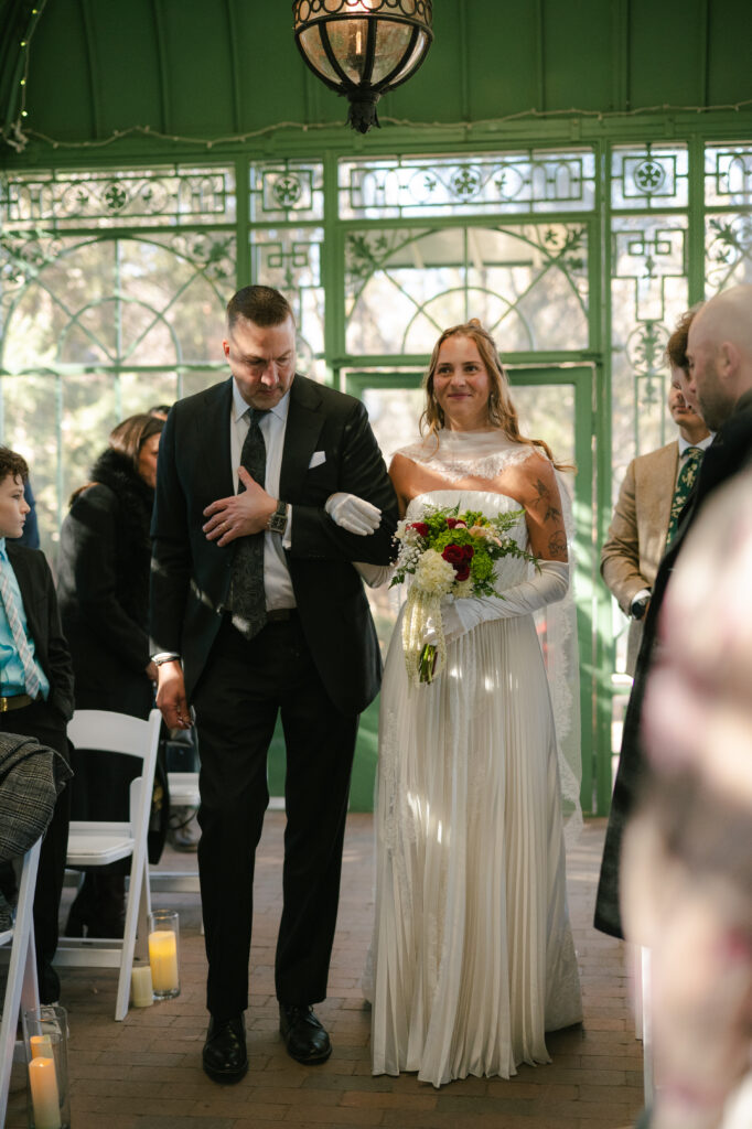 Bride walking down the aisle with her father in a greenhouse