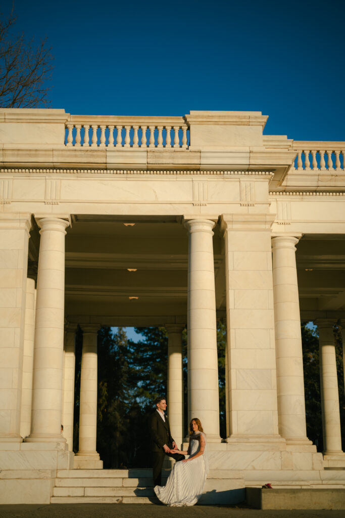 Bride and groom looking at camera from far away in front of columns