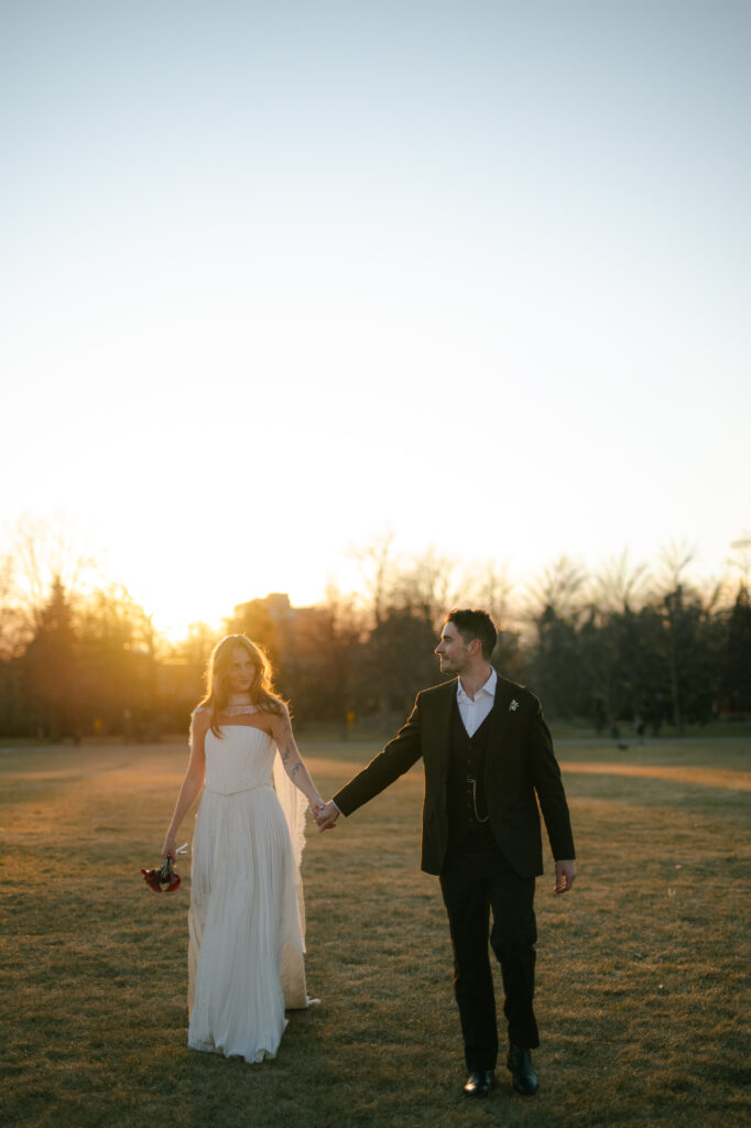 Bride and groom walking towards camera holding hands in golden hour light